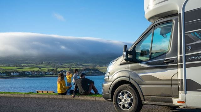 Family sitting outside motorhome parked by a lake